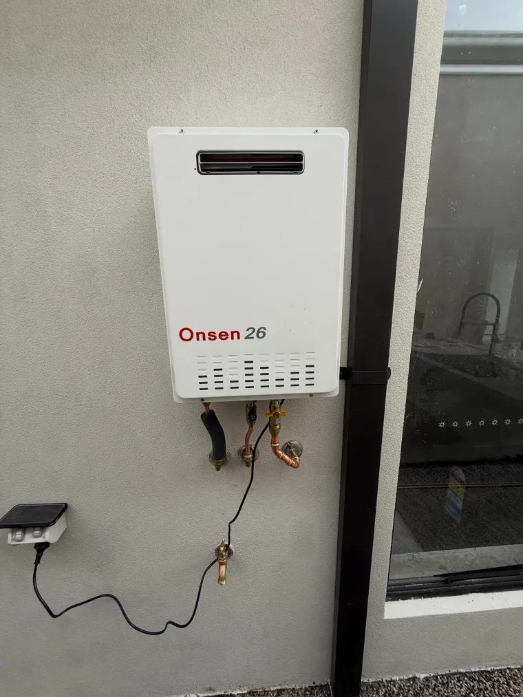 Wall-mounted instantaneous gas hot water unit with copper connections and an isolation valve below it